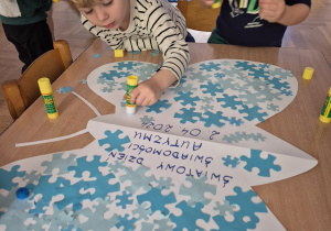 Dzieci podpisują obrazki z niebieskimi puzzlami.