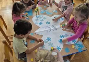 Dzieci siedzace przy stolikach kolorują obrazki na niebiesko.